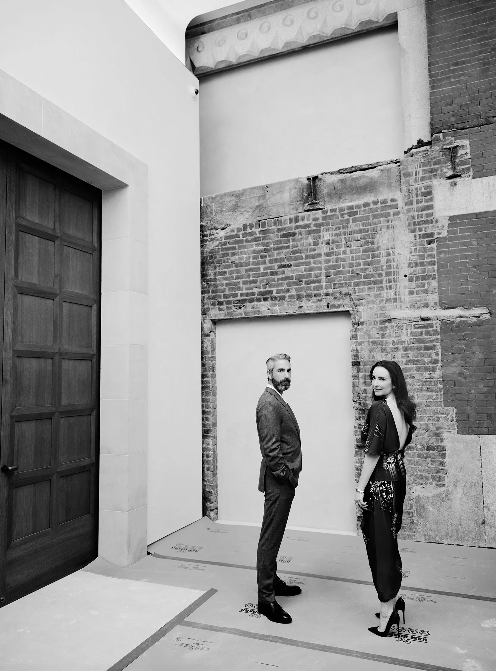 Image may contain Adult Person Clothing Pants Formal Wear Suit Walking Door Accessories Bag and Handbag